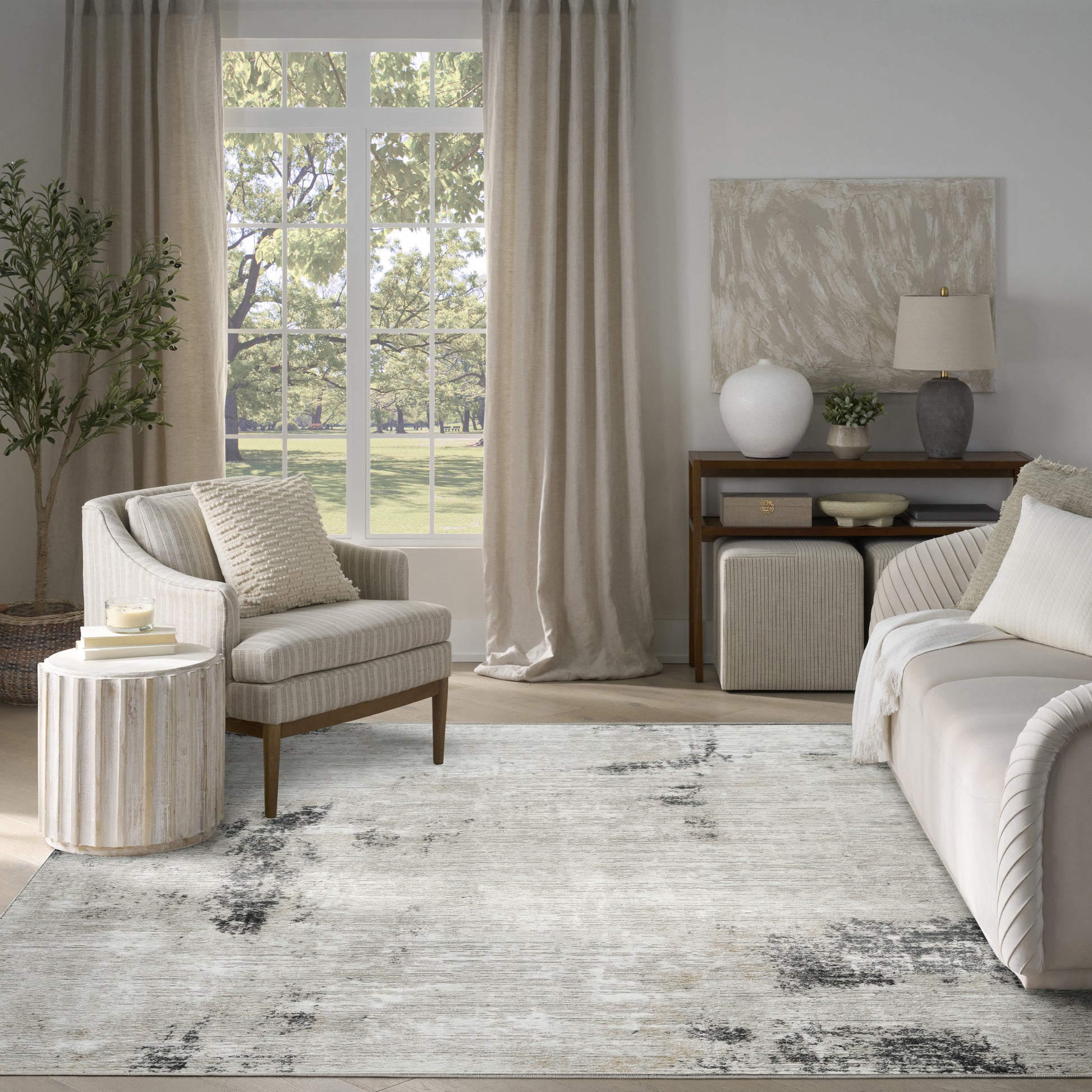 Neutral living room with beige sofa, striped armchair, round ribbed wood side table, soft cushions, light rug, curtains.
