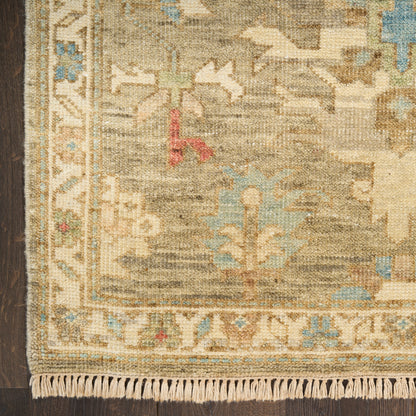 Close-up of a beige, Persian-style rug with blue accents, ornate border and fringed edge on a dark wood floor.