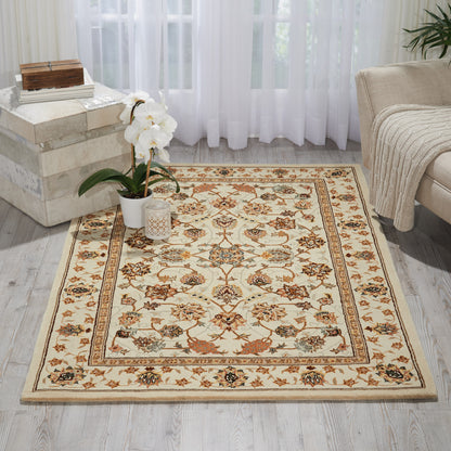 Cream floral area rug with ornate beige border, orange accents, on light wood floor beside a potted orchid and beige sofa.