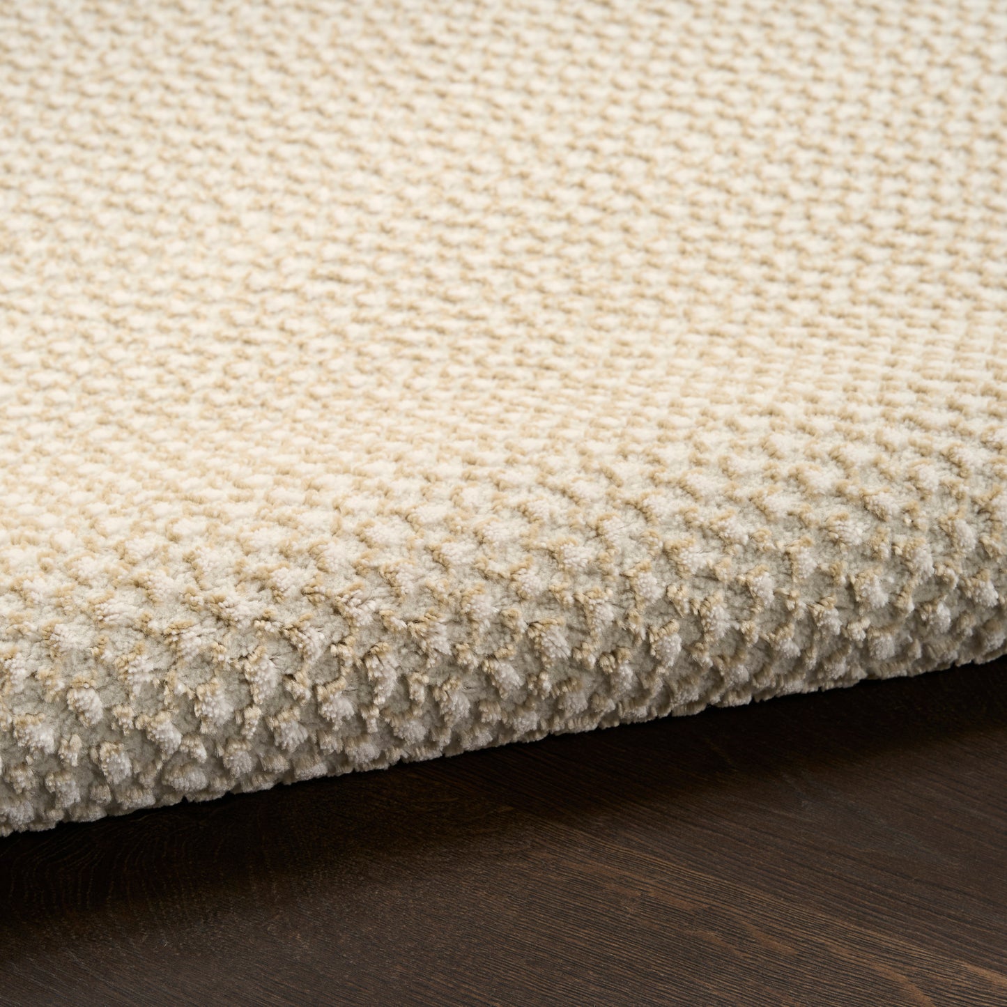 Beige textured loop-pile rug with dense plush fibers, shown edge-on on dark wood floor.