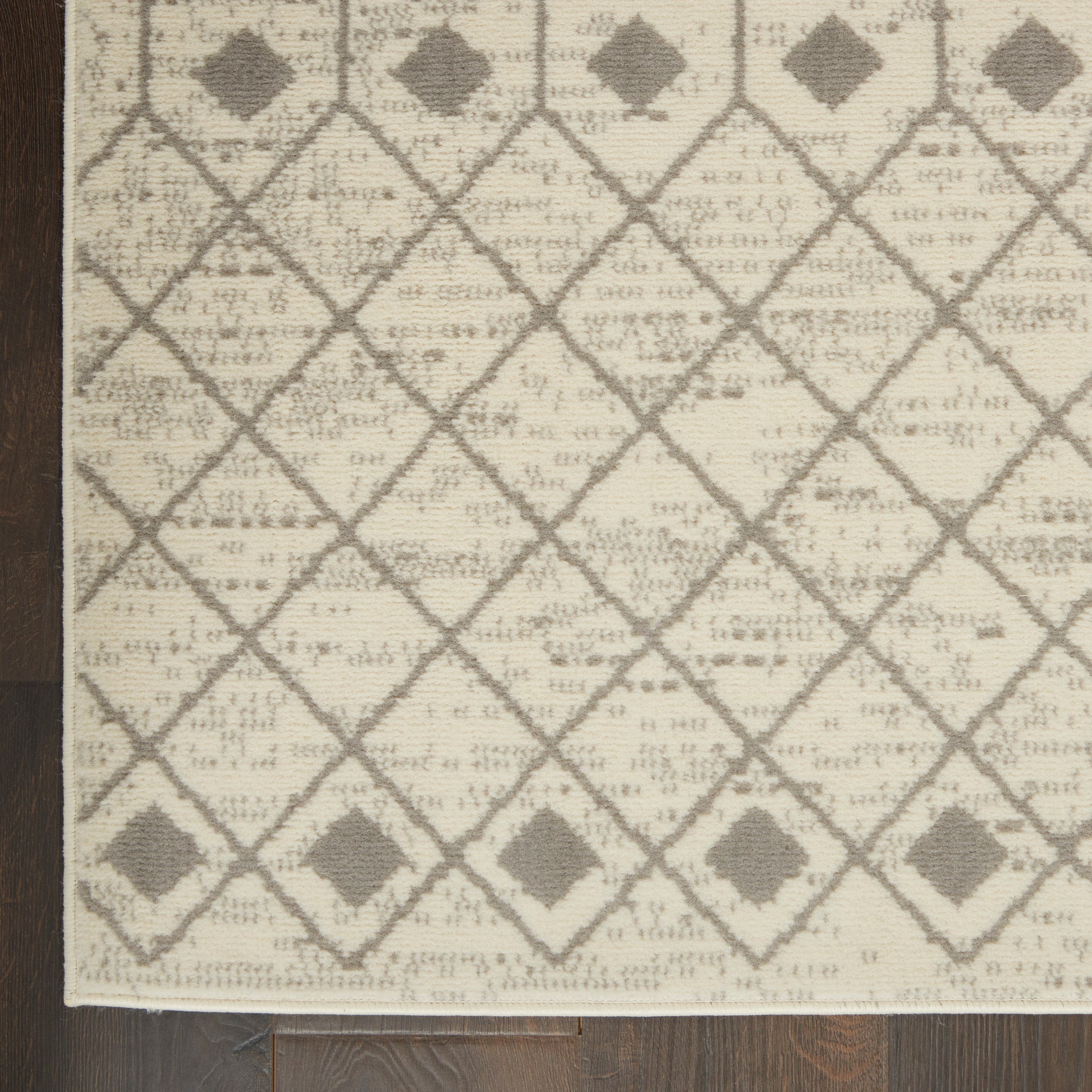 Beige woven rug with gray diamond lattice pattern, small diamonds at intersections, light fringe along edge.