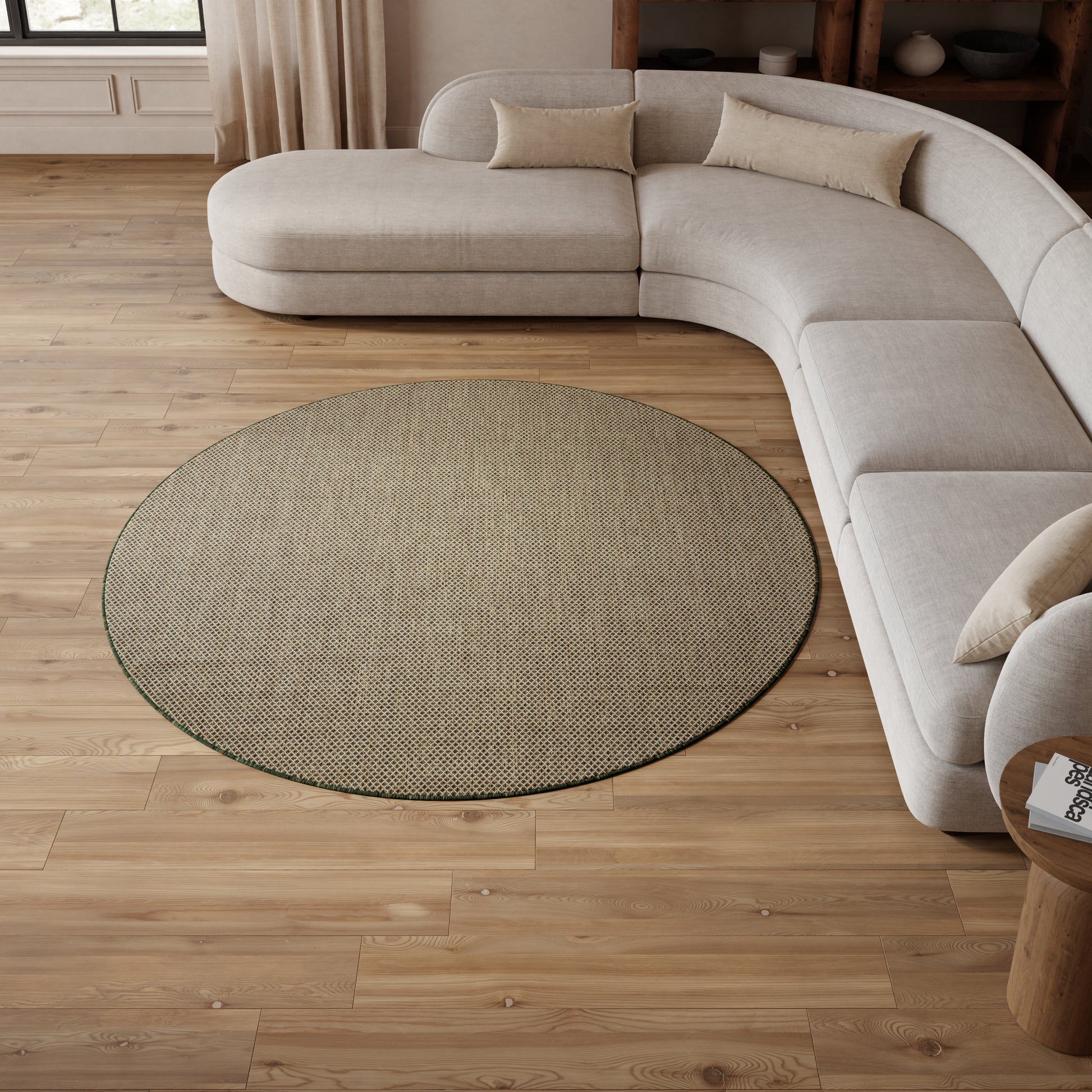 Light gray curved sectional sofa with beige pillows around a round woven rug on warm wood floors in a bright living room.
