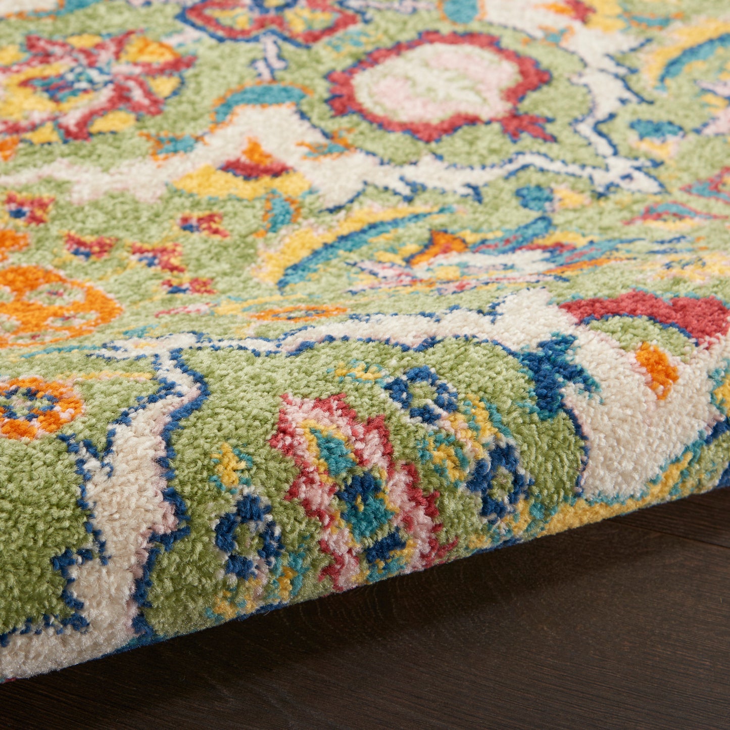 Close-up of a vibrant multicolor rug with a green base, floral motifs, and soft fluffy pile on dark wood.