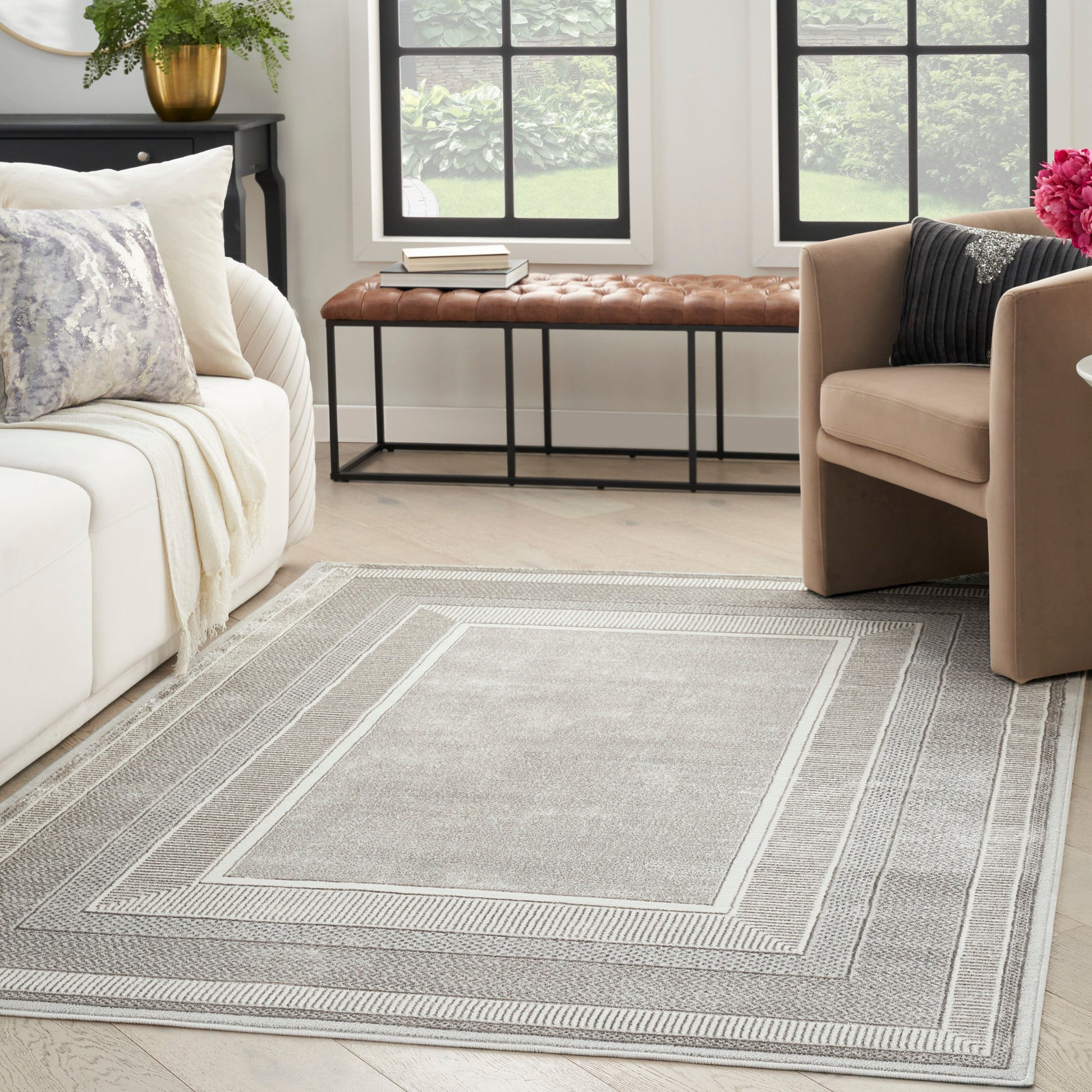 Grey woven area rug with layered geometric borders in a modern living room & beige sofa & tan armchairs.