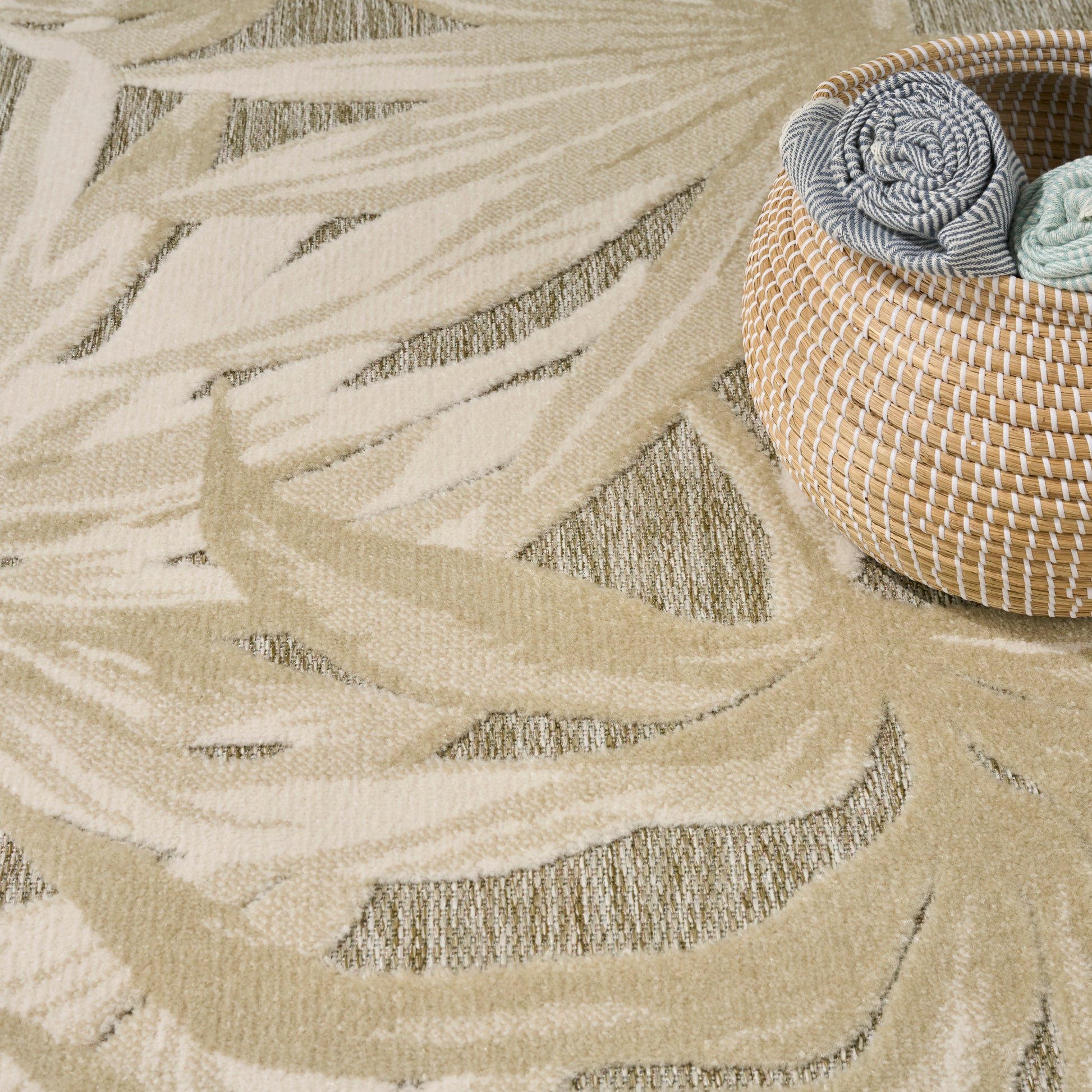 Beige and cream abstract leaf rug with a round wicker basket with rolled blue and green towels.