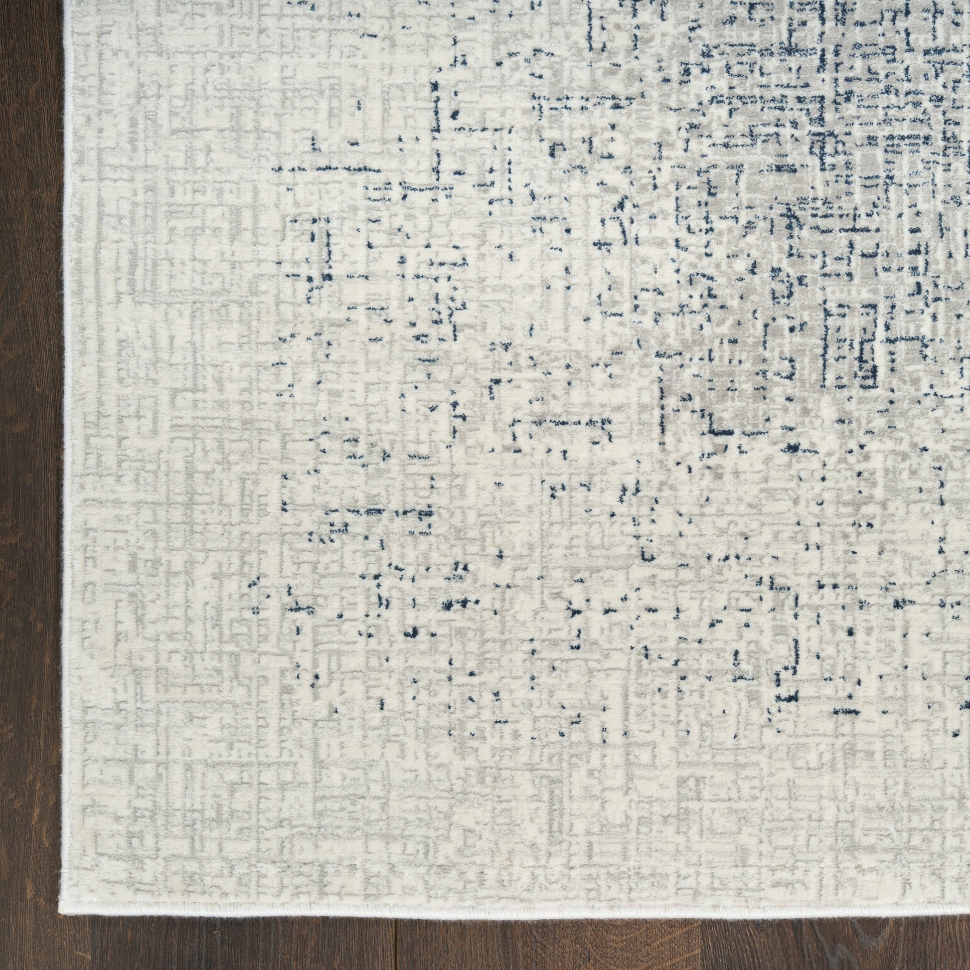 Cream ivory area rug with subtle blue-gray geometric distressed pattern on dark hardwood floor.