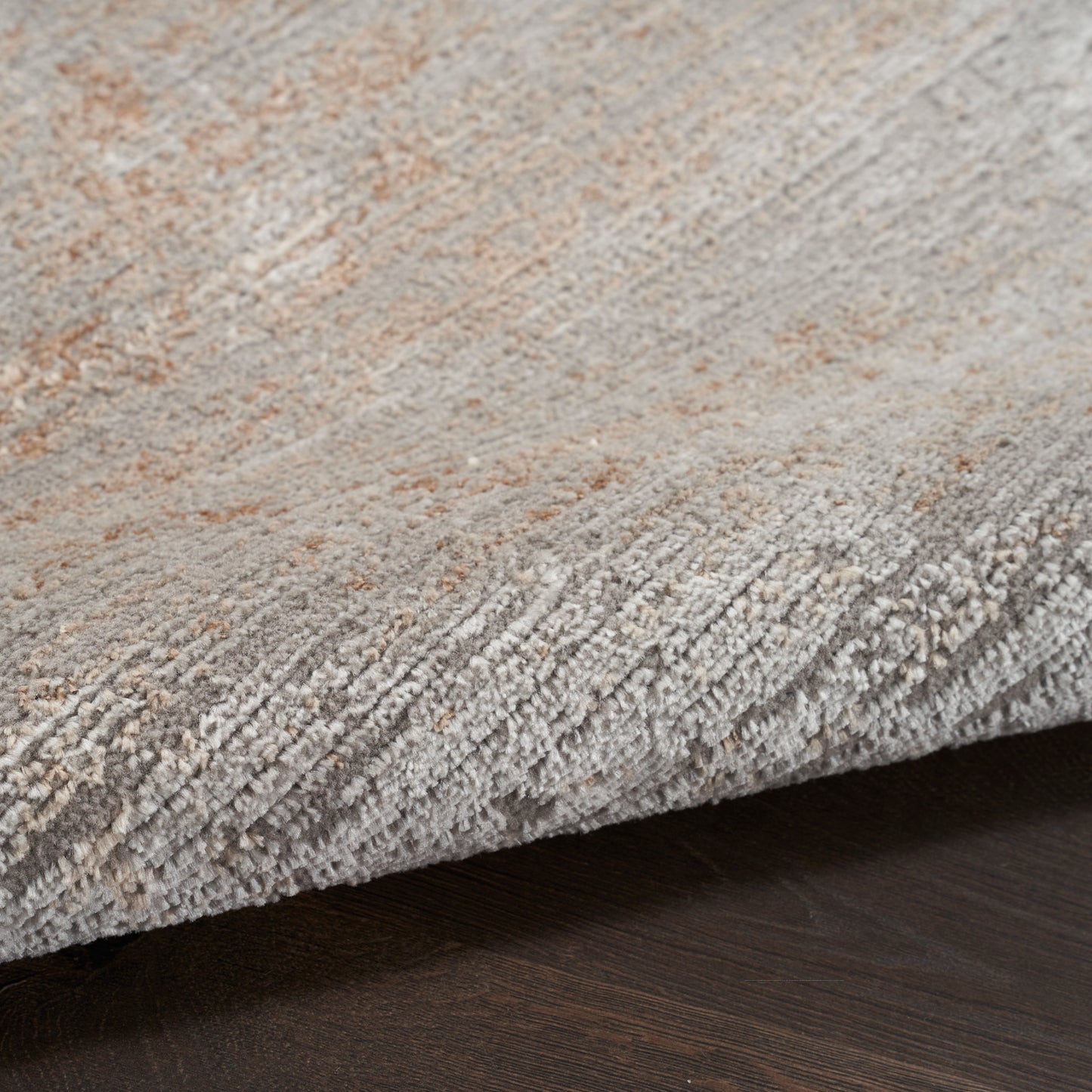 Textured abstract area rug in light gray, beige and taupe tones with plush cut-pile, curled edge on dark wood floor