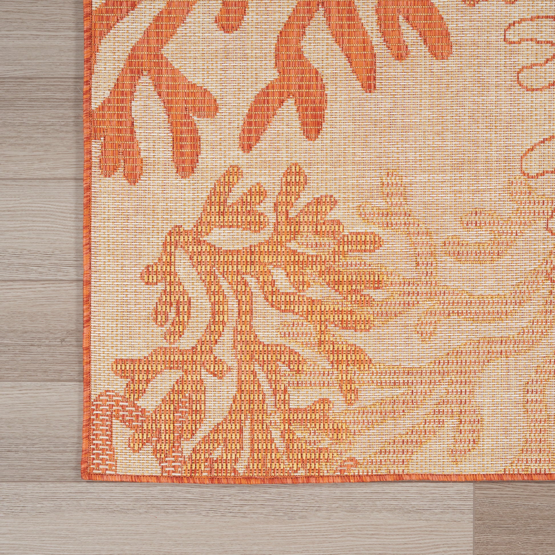 Orange botanical rug with light beige background and thin orange border, spread over wood flooring.