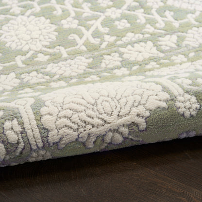 Olive green rug with white raised floral damask pattern, soft plush pile on dark wooden floor.