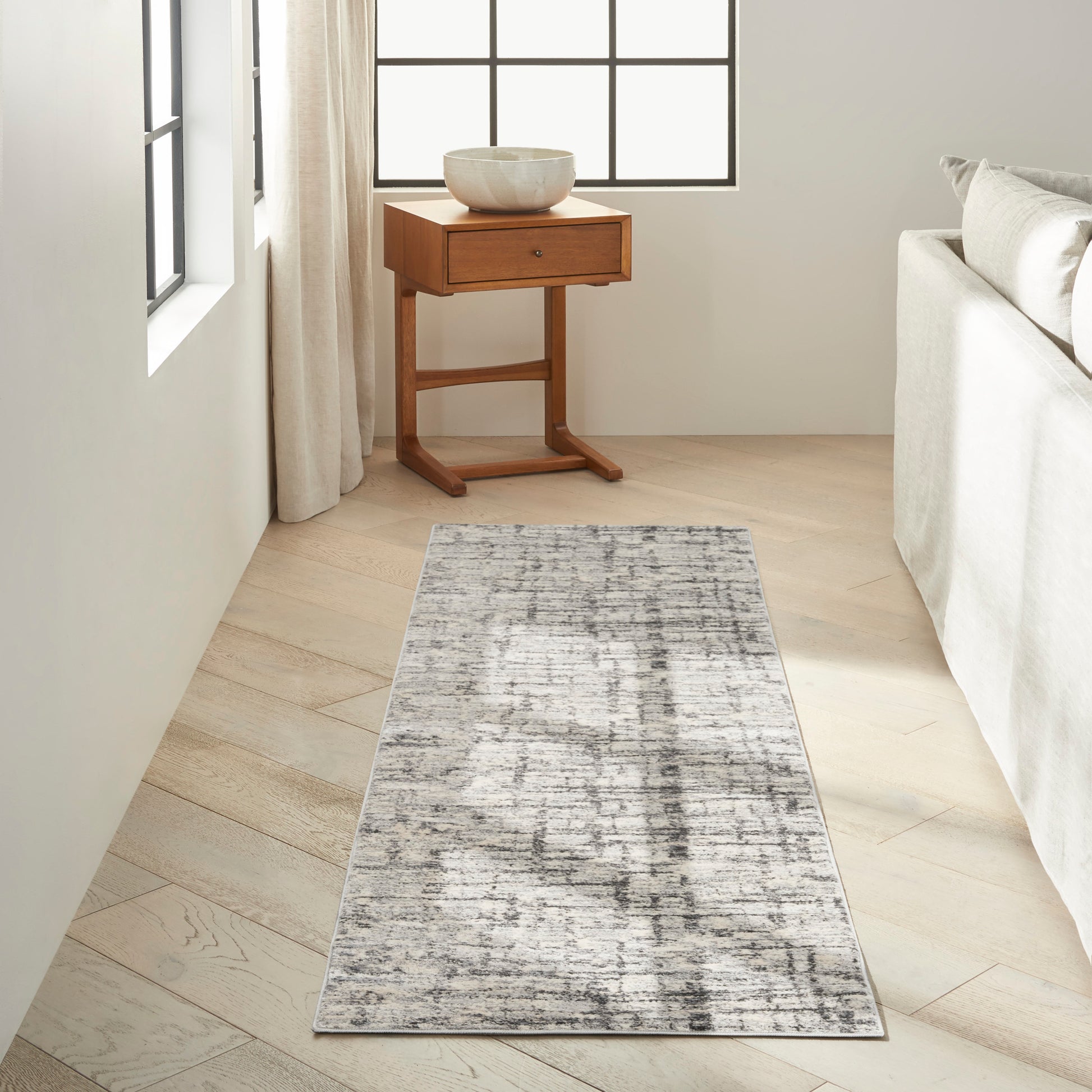 Bright neutral living room with a gray abstract-pattern runner rug, beside a wooden side table & a ceramic bowl.