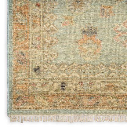 Muted teal oriental rug with cream border, peach floral motifs, woven texture and fringe along edge.