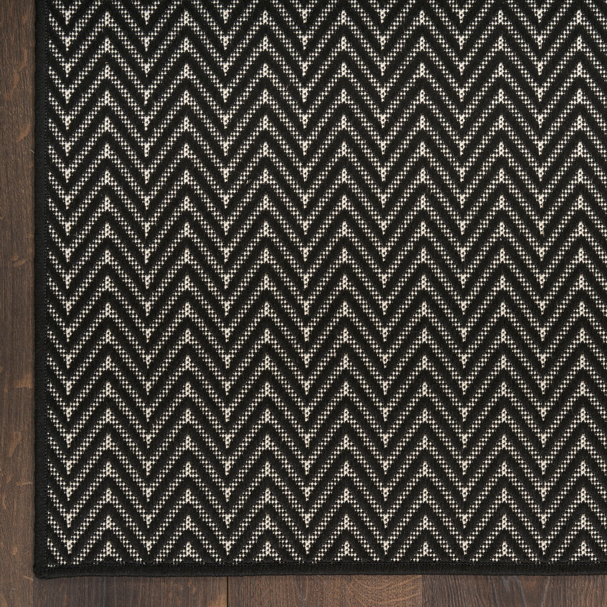 Black & white chevron rug with a textured weave on a dark wood floor, bordered in black.