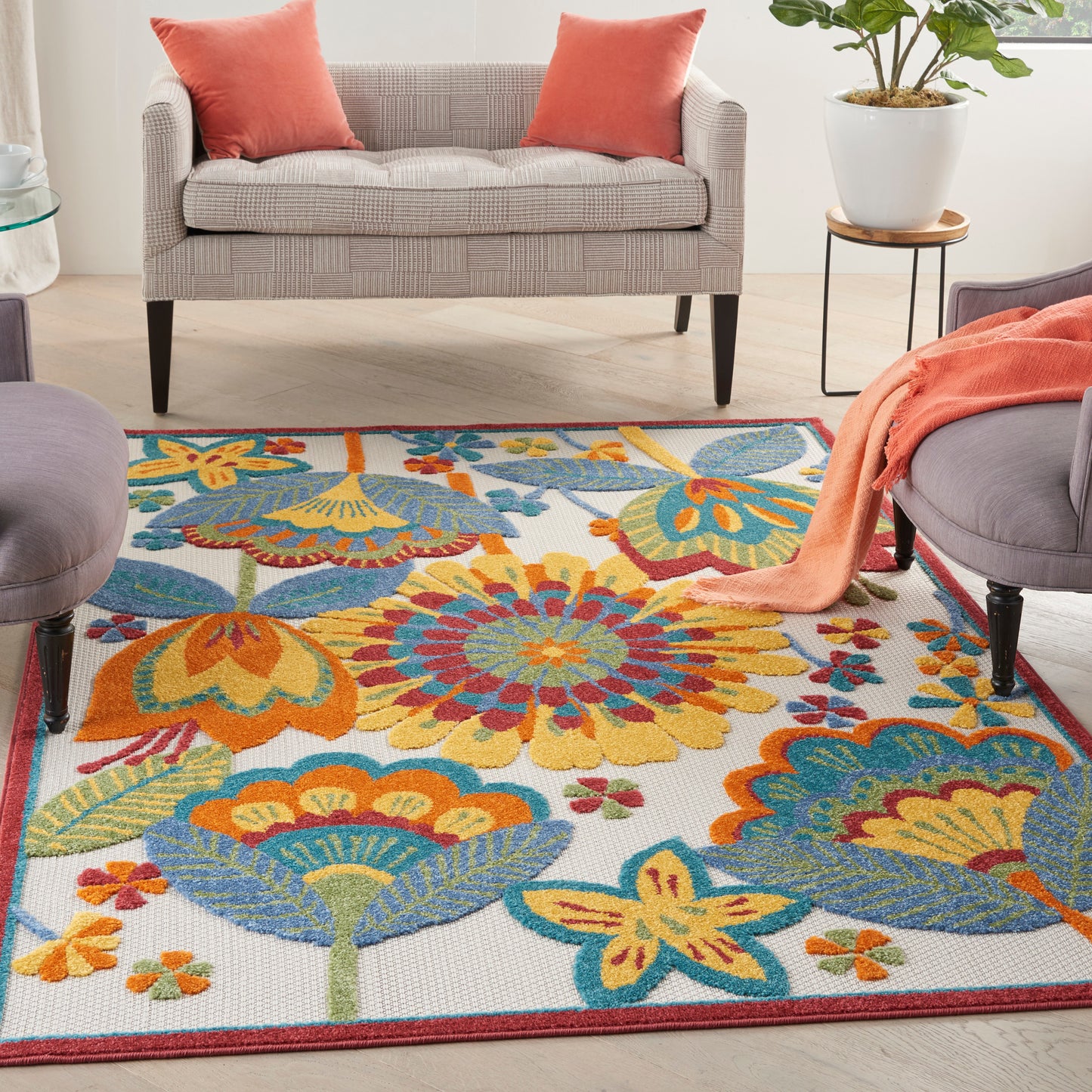 Vibrant floral area rug on light floor with gray sofa, coral cushions, gray chairs, a potted plant, and orange throw.