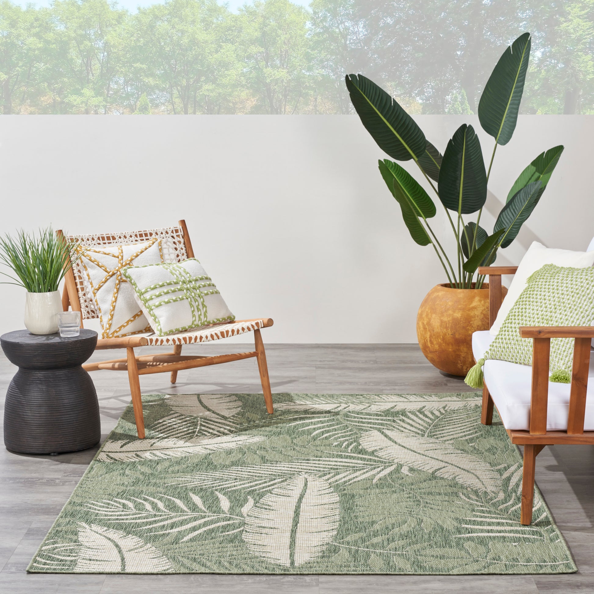 Green palm-leaf patterned rug on a wooden patio with mid-century chairs and a tall potted plant.