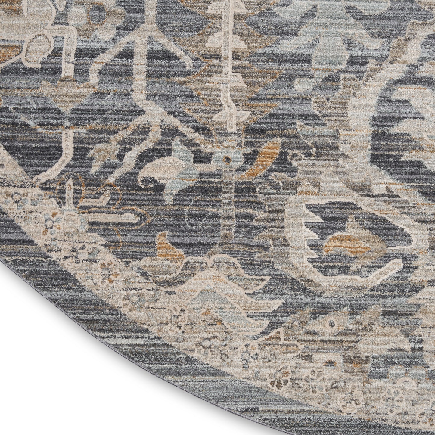 Distressed blue-gray round rug with beige and pale blue floral vine pattern; curved edge shows folded edge.