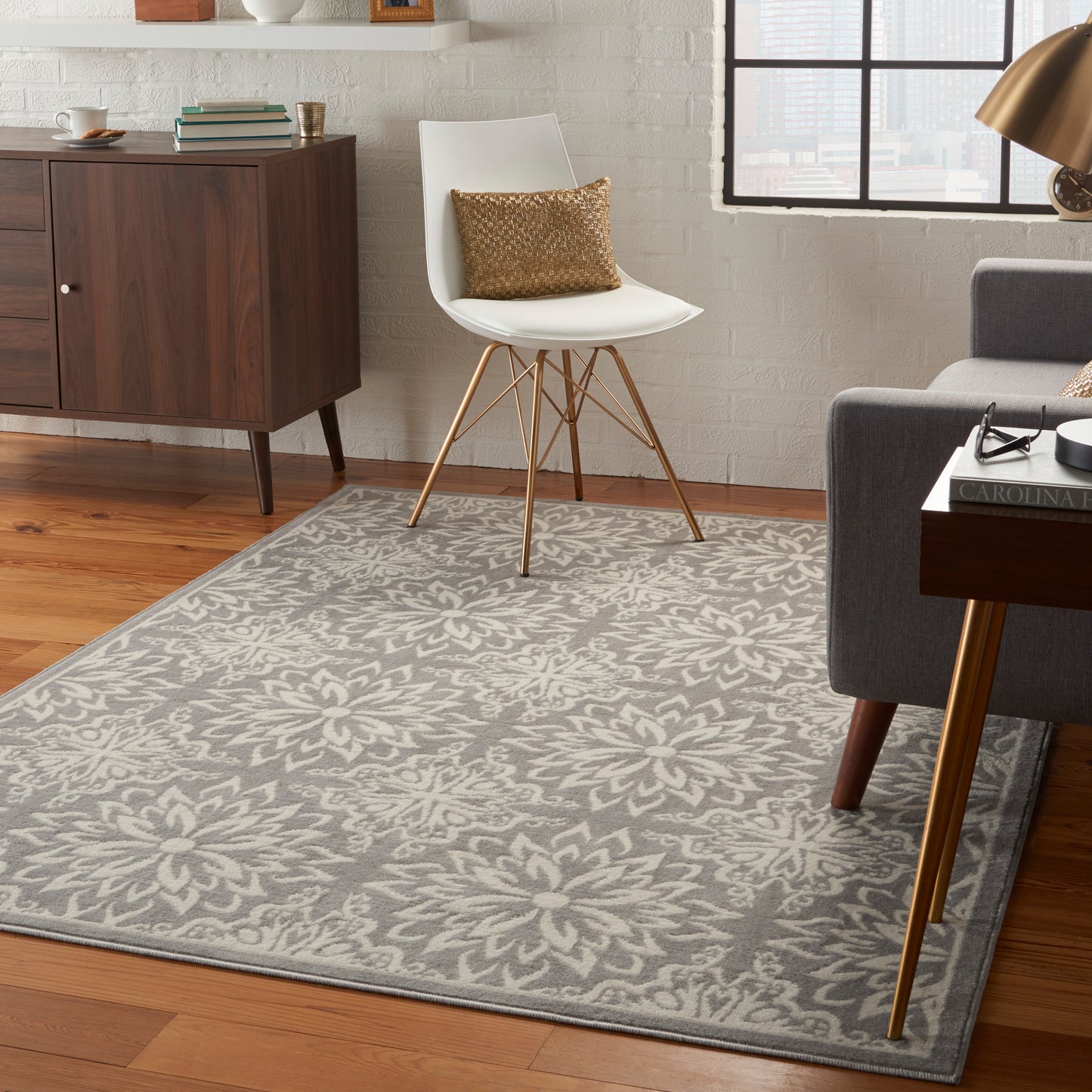 Gray floral area rug on wooden floor with mid-century white chair, dark wood credenza, and grey sofa in modern living room.