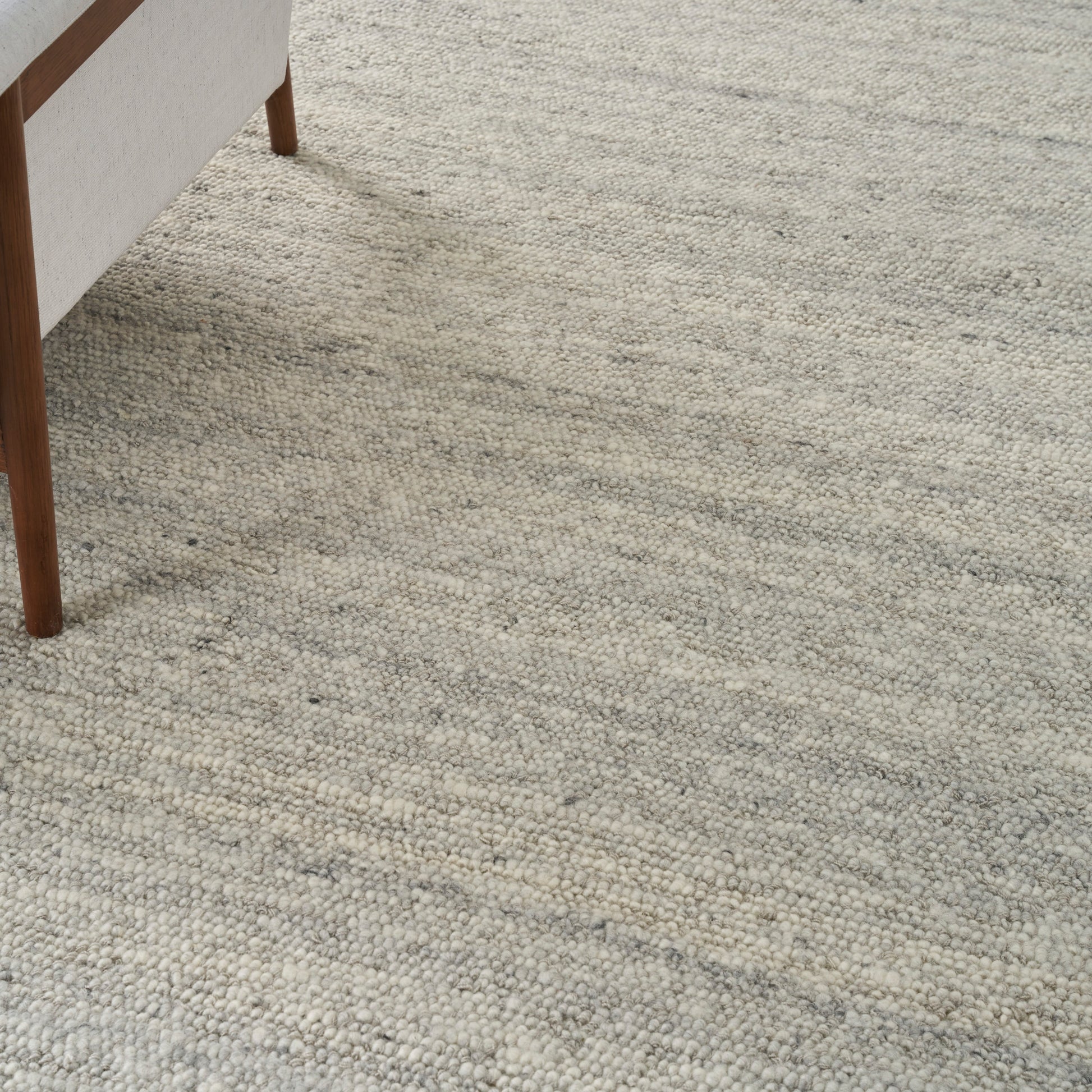 Beige speckled loop-pile rug with a wooden sofa leg visible.