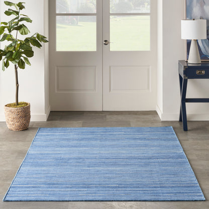 Blue striped flatweave entryway rug on wood floor, with potted plant and console table by double doors.