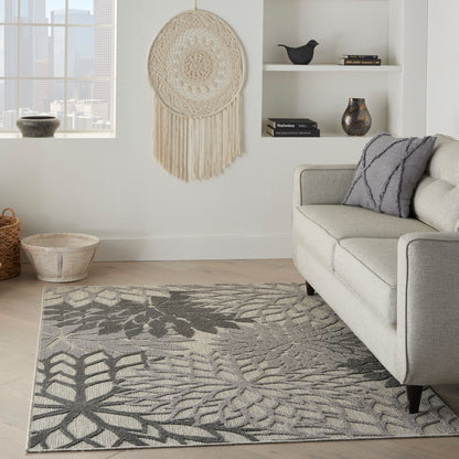 Boho-modern gray botanical area rug on light wood floor with a light gray sofa, macramé wall hanging, woven baskets and minimalist shelves.