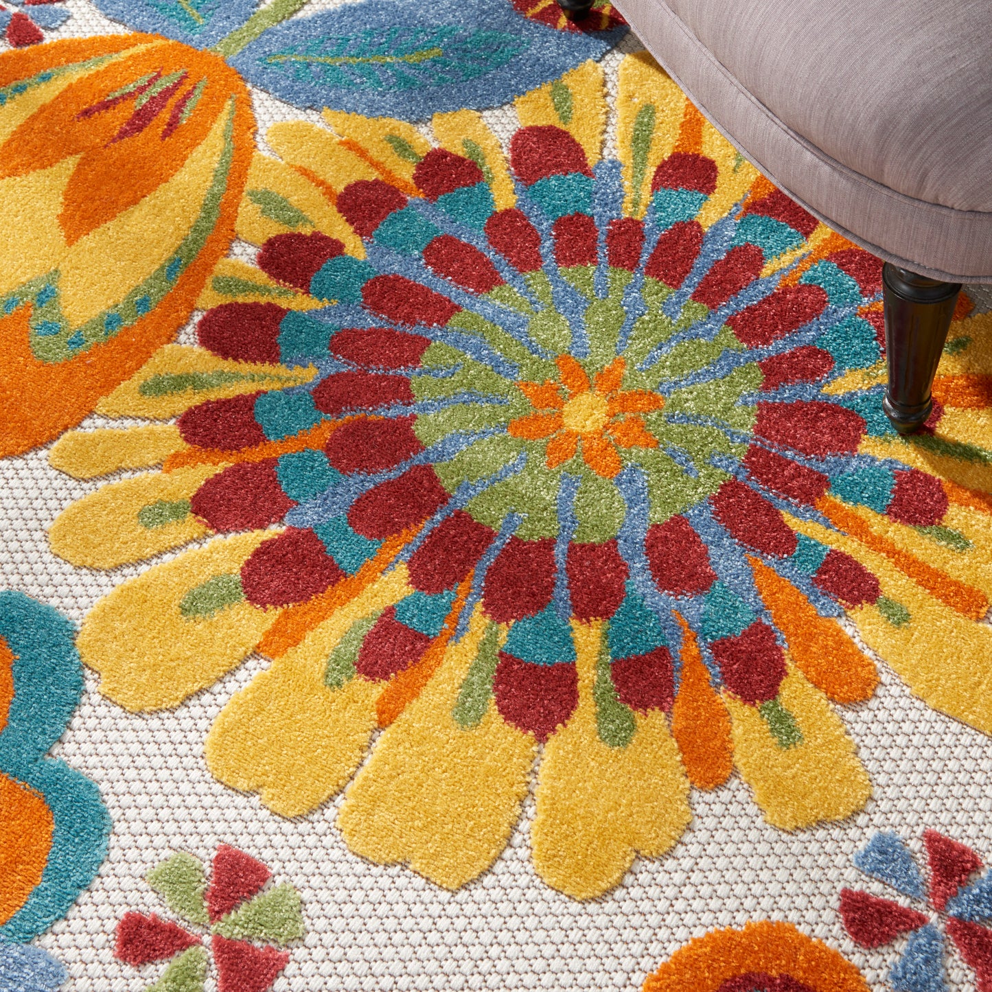 Bright multicolor circular floral rug with yellow, orange, red and turquoise petals; beige chair leg nearby.