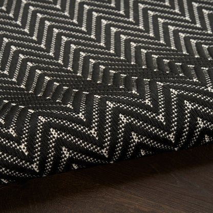 Black and white chevron woven rug with a bold zigzag pattern, folded on a dark wood surface.