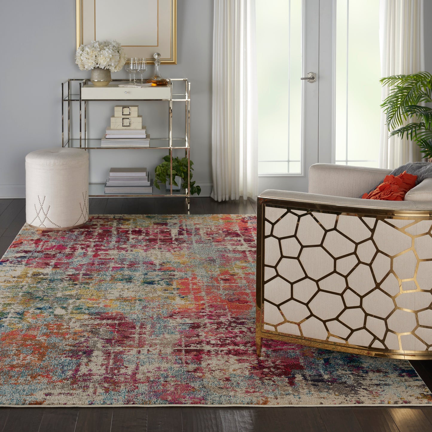 Vibrant distressed multicolor area rug on dark wood floor in a modern living room with gold honeycomb chair and glass console.