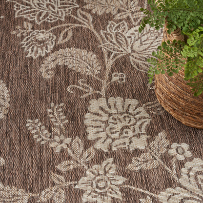 Brown woven rug with cream floral pattern; textured weave, near a wicker plant basket.
