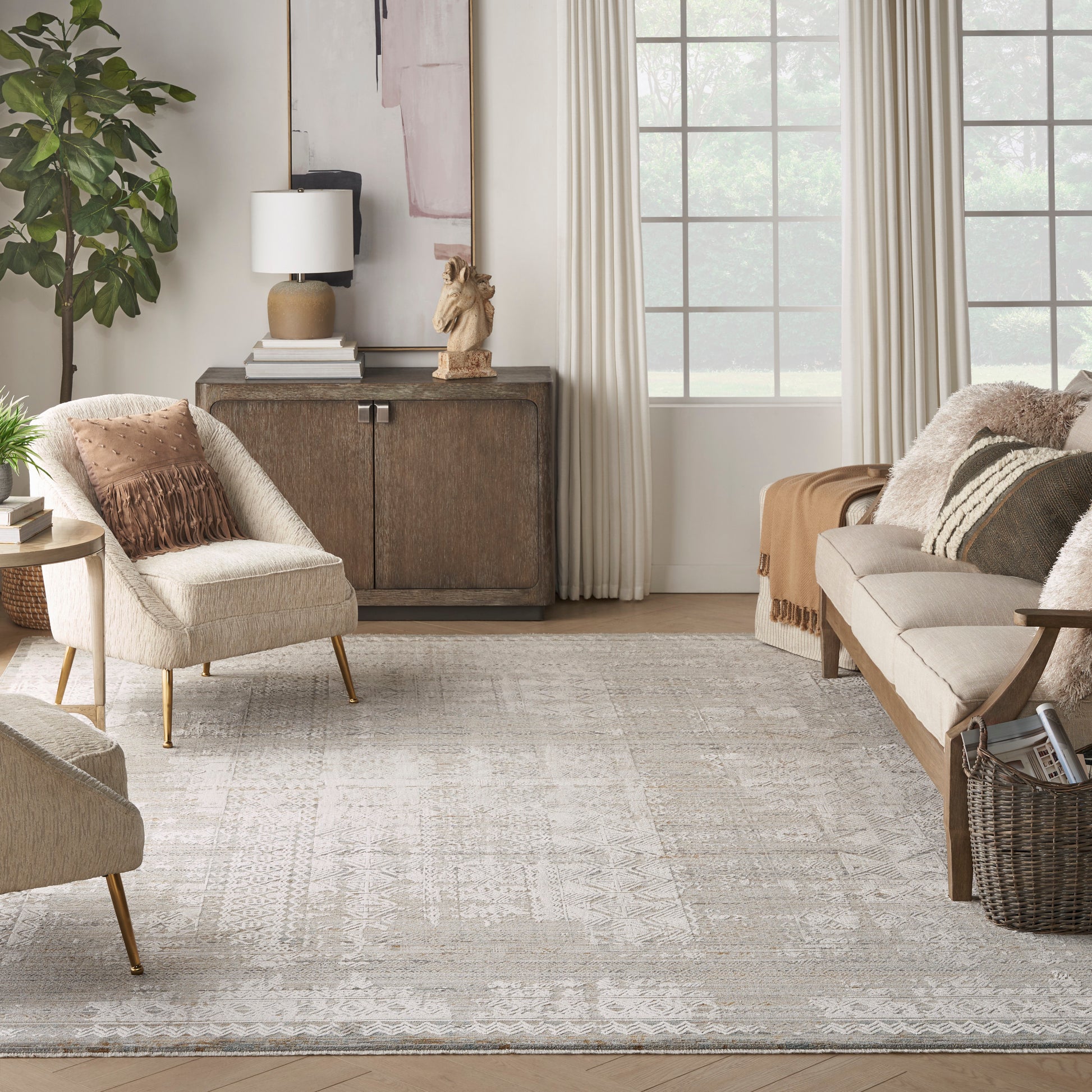 Neutral living room with cream tufted chairs, tan sofa, wooden cabinet, soft patterned rug, plants, and cozy throws.