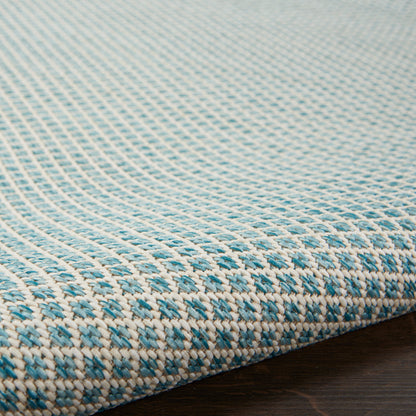 Close-up of a blue and white woven rug with a tight checkered pattern and textured fabric on a dark wooden floor.