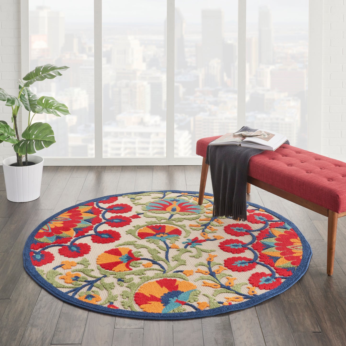 Round floral rug with red, blue, yellow and green on beige, blue border, in a bright living room with a red tufted bench.