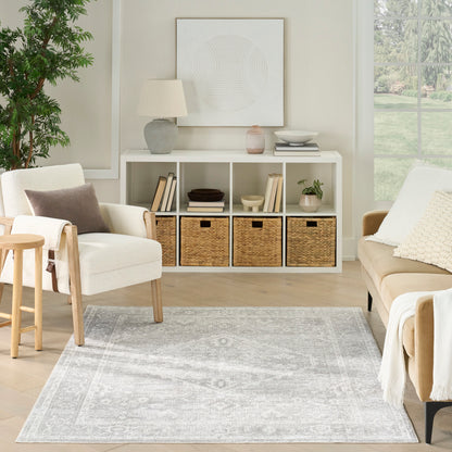 Bright living room with a gray 5' x 7' rug, beige sofa, cream armchair, white cubby shelves, woven baskets, and a light wood stool.
