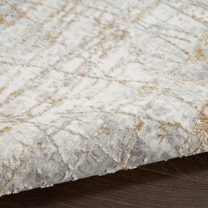 Close-up of a plush gray area rug with beige and gold geometric pattern resting on dark wood floor.