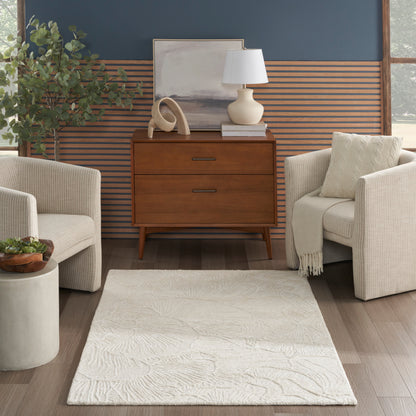 Mid-century walnut dresser with two drawers, flanked by beige armchairs, cream rug, plant, and blue slat-wall backdrop.