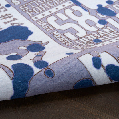 Light lavender fabric with blue abstract florals and white line-art text motif, folded on dark wood.