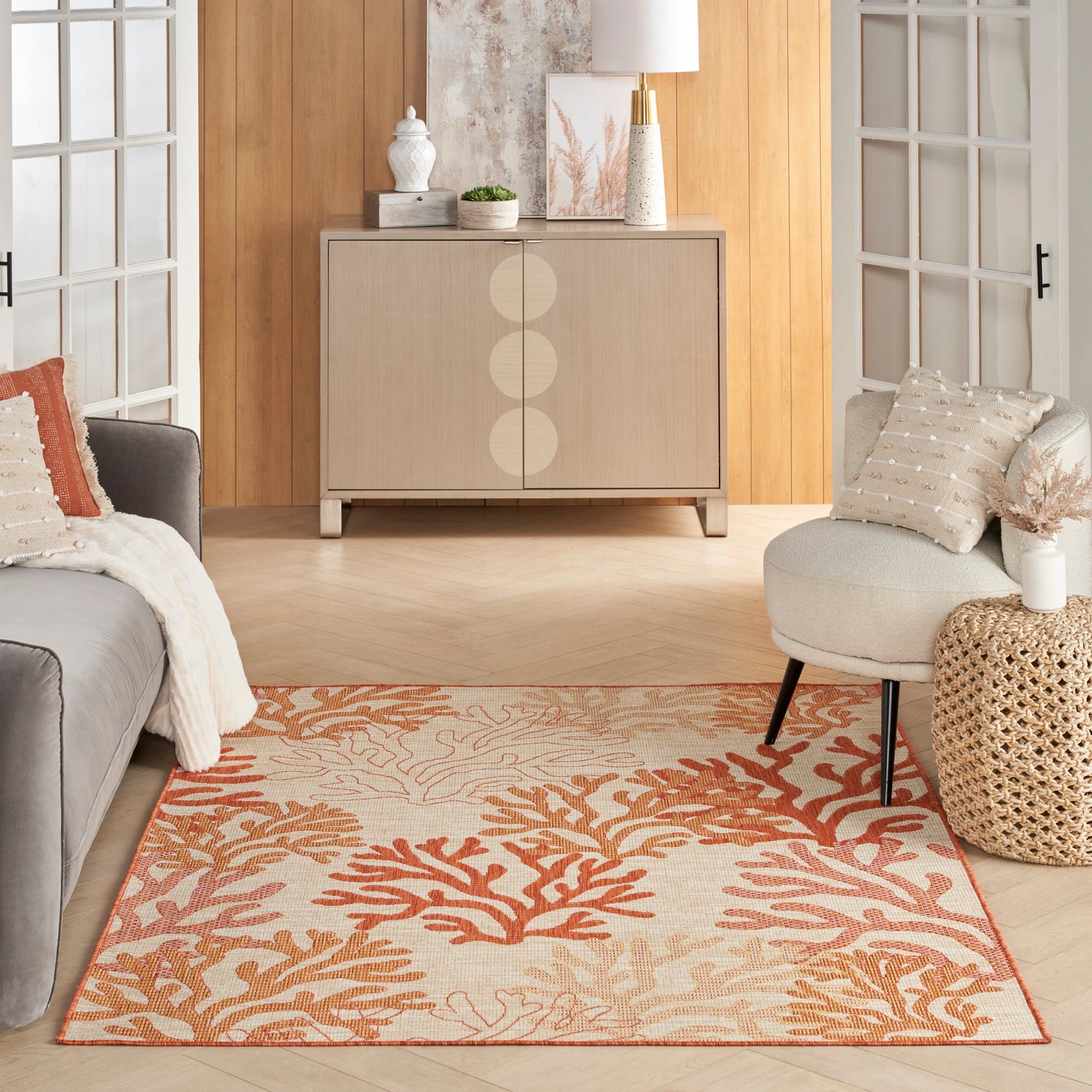 Orange coral-pattern area rug on cream background in a modern mid-century living room with beige cabinet and gray sofa.
