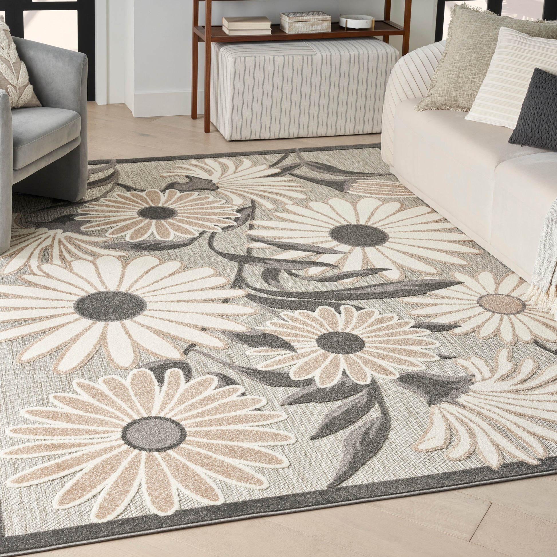 Large floral area rug with beige and gray daisies on a light neutral background in a modern living room.