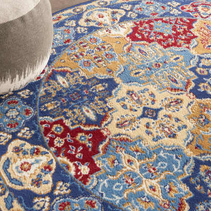 Close-up of a Persian-style area rug in blue, ivory, red & gold with floral medallions; light gray ottoman visible.