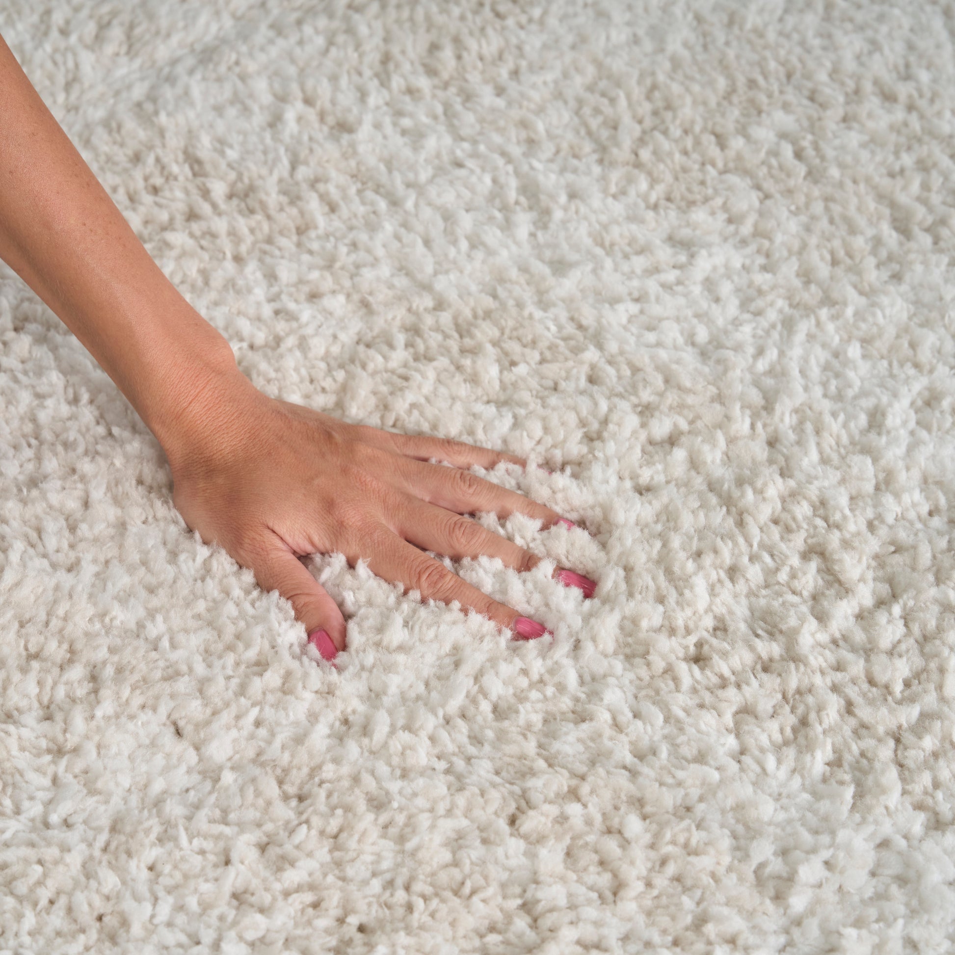 Hand pressing on plush white shag rug; fluffy pile, pink nails, cozy home decor floor rug.