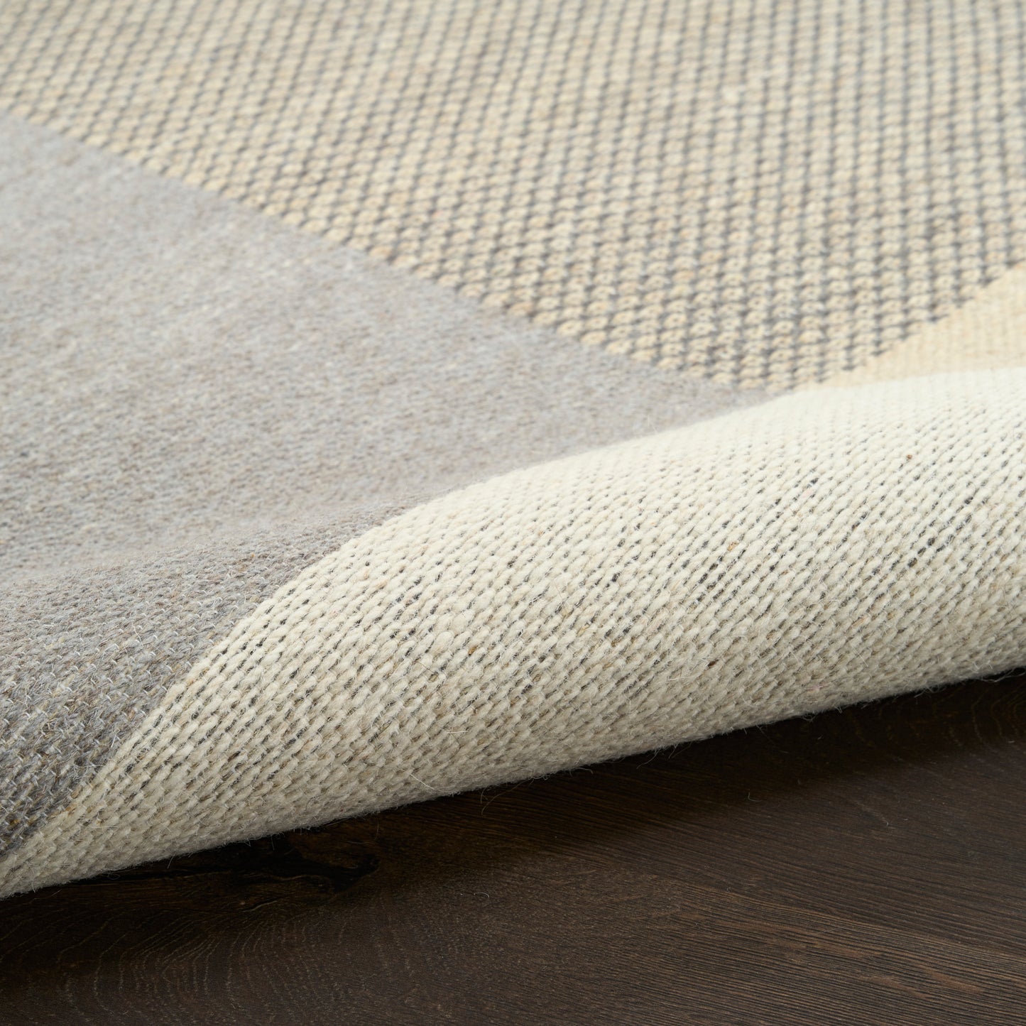 Two-tone woven rug in gray & beige on a dark wooden floor; folded corner reveals soft underside.
