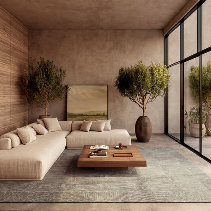 Beige modular sofa with cushions in a warm, contemporary living room; wooden coffee table, rug, potted trees, and glass wall.