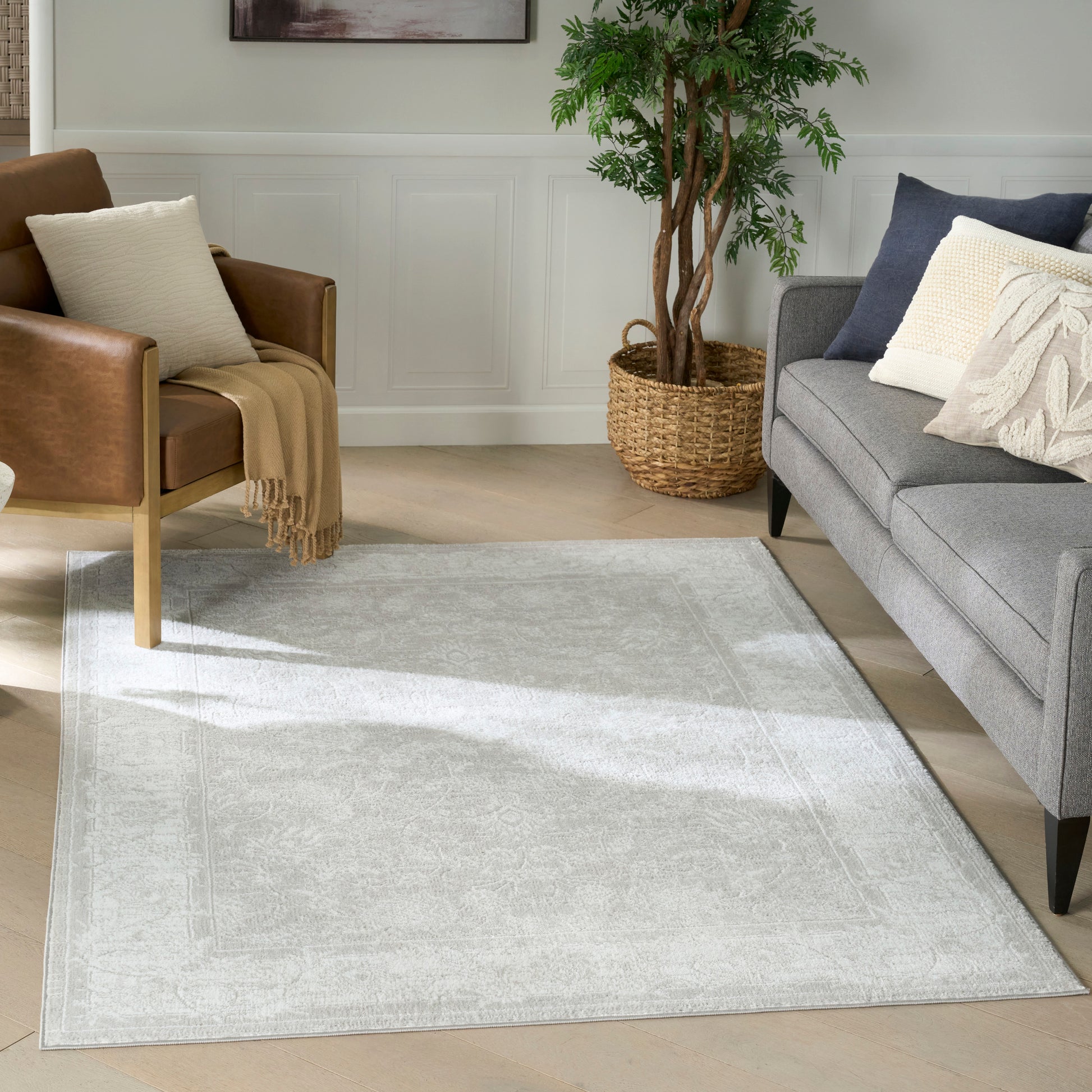 Light gray patterned rug anchors a modern living room with gray sofa, brown leather chair, beige throw, and potted plant.