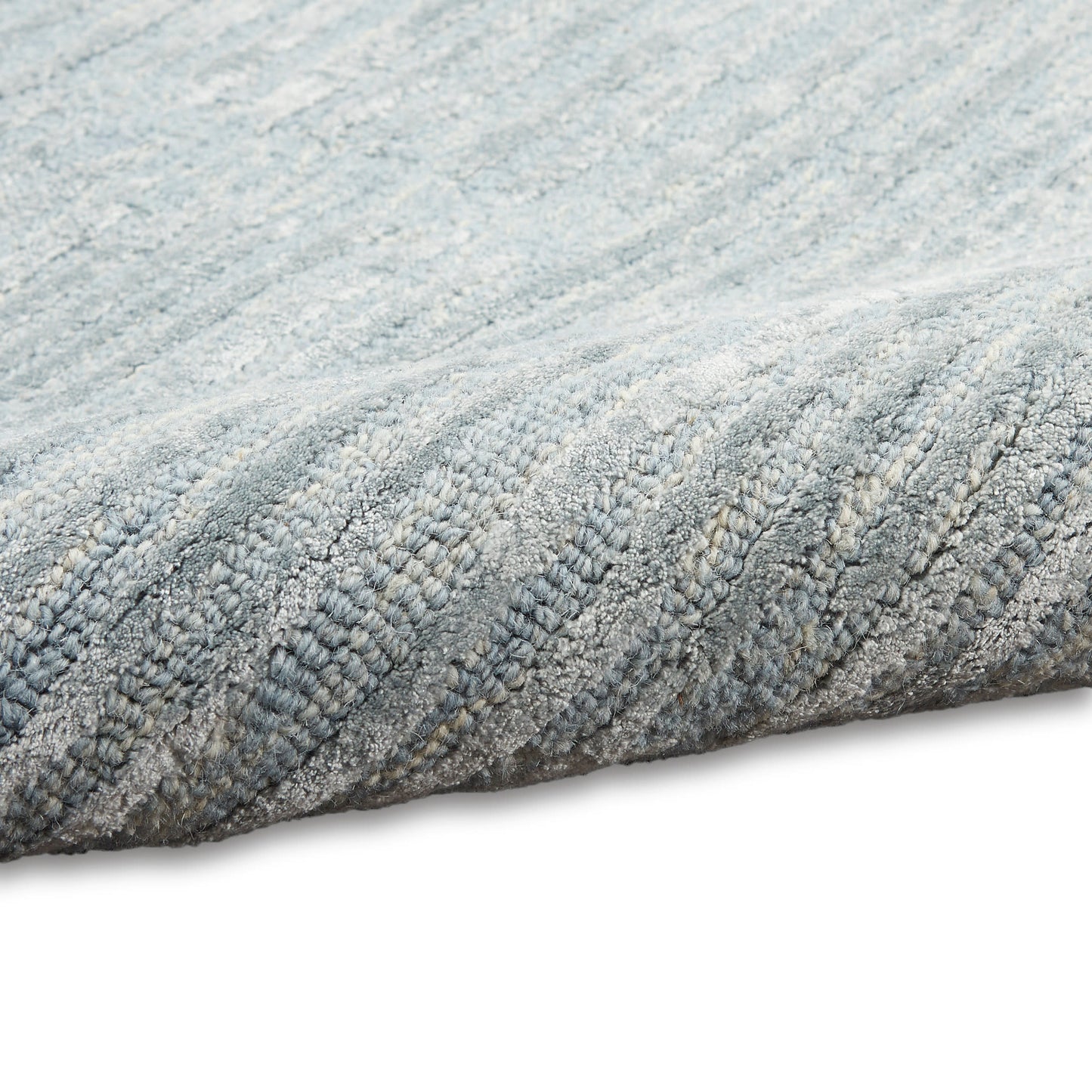 Close-up of a soft grey-blue textured rug with a ribbed loop pile and rolled edge.