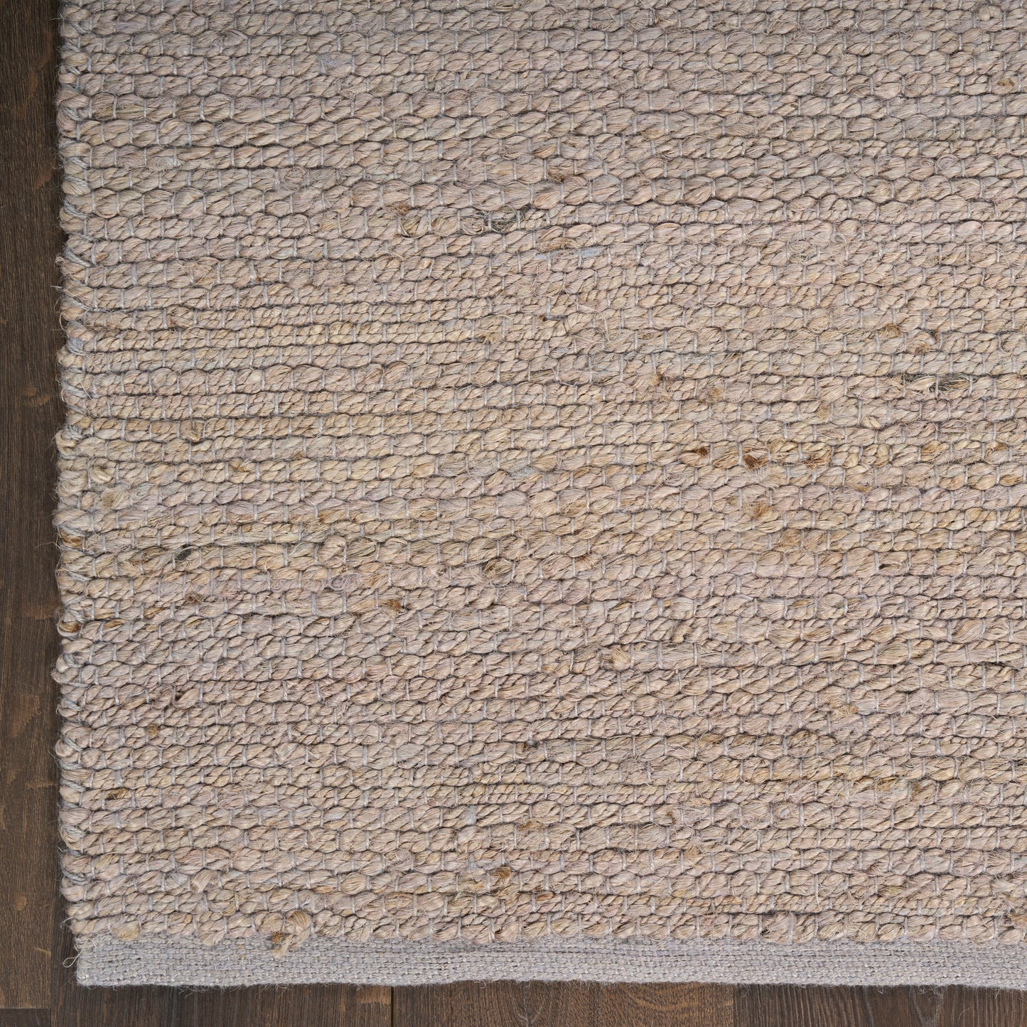 Beige textured woven rug with loop pile and dark edge trim on a wooden floor; cozy neutral rug for living spaces.