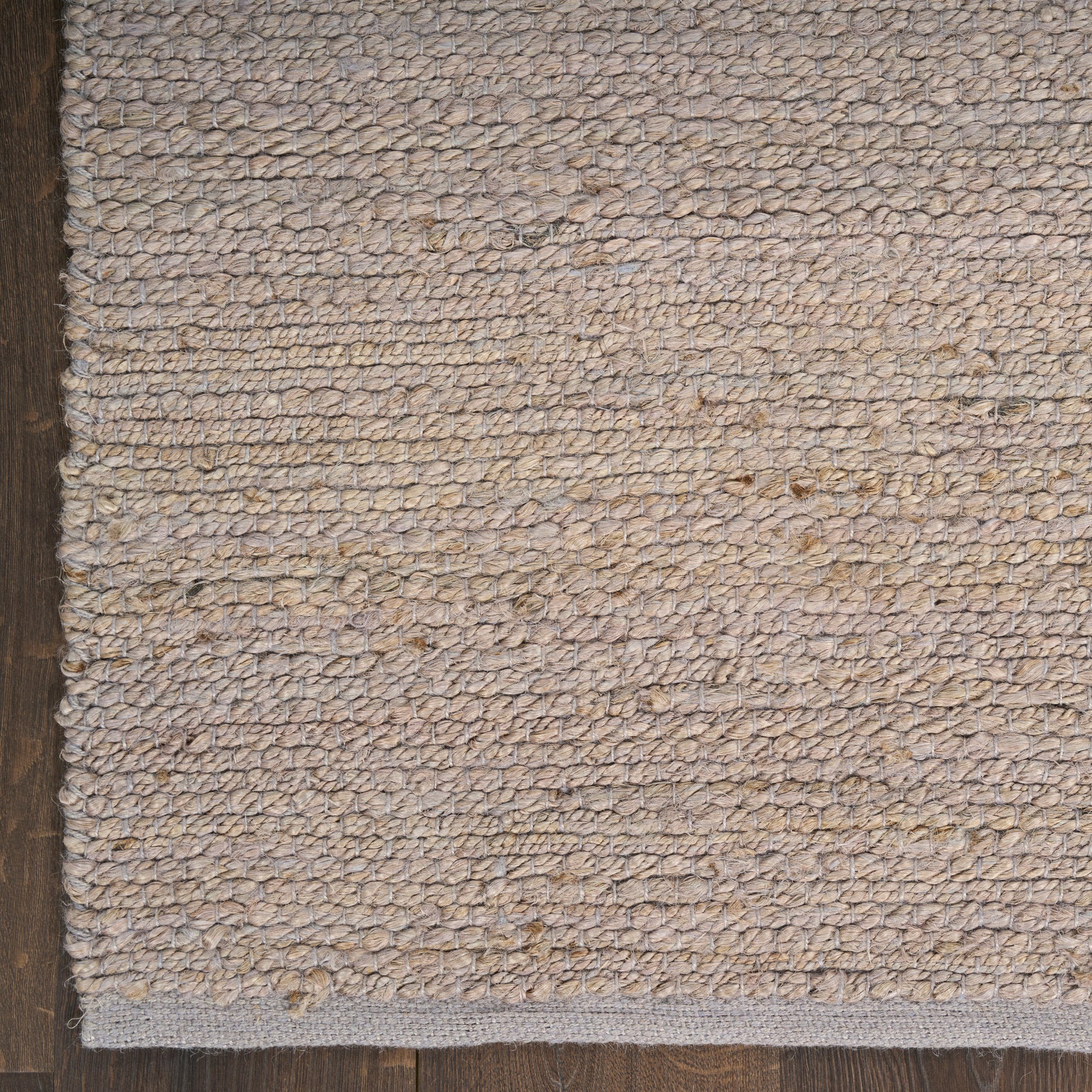 Beige textured woven rug with loop pile and dark edge trim on a wooden floor; cozy neutral rug for living spaces.