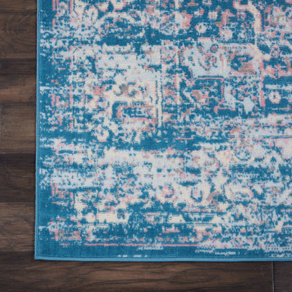 Rectangular blue distressed rug with pink and ivory faded pattern, teal bound edge on dark wood floor.