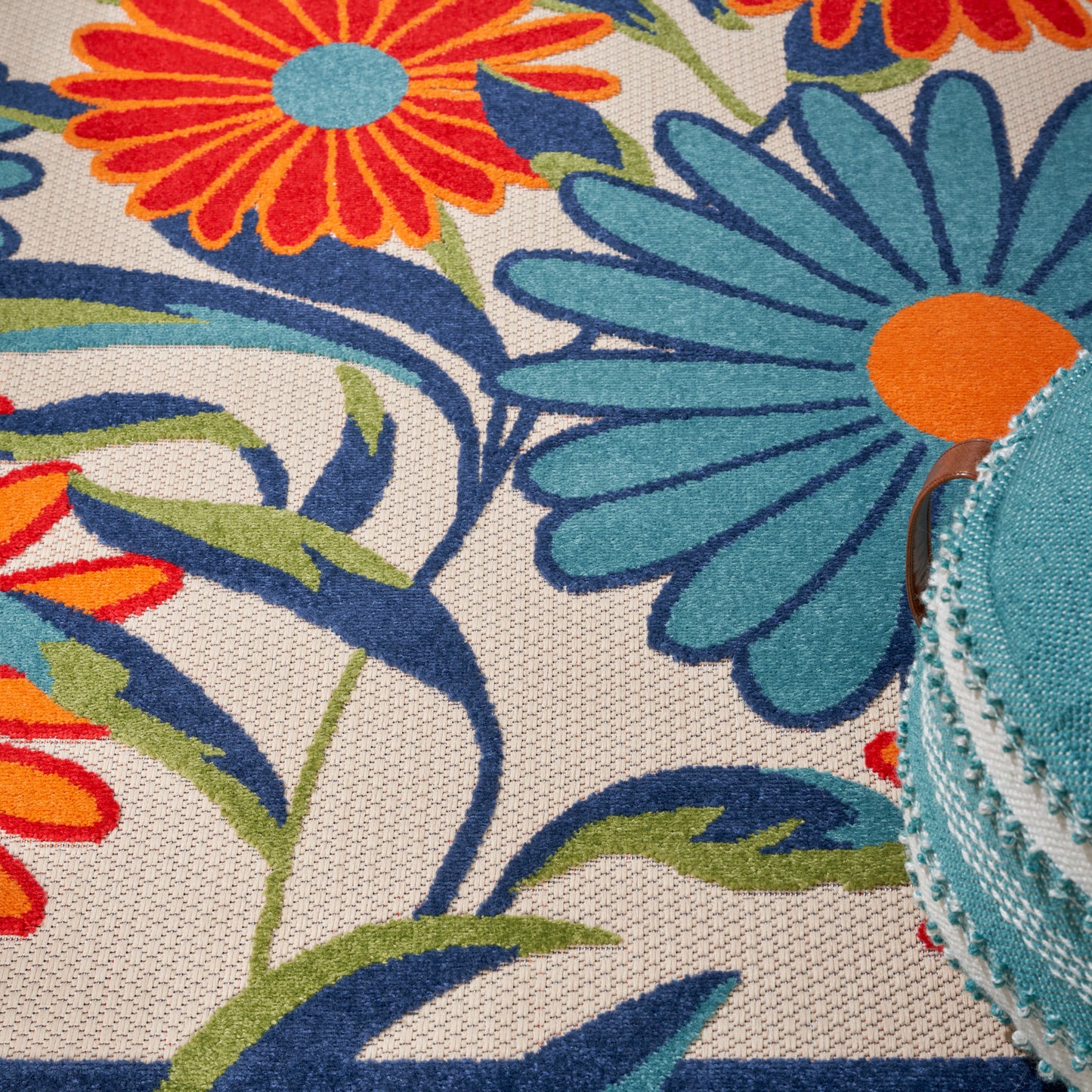 Bright floral rug pattern with orange, teal and blue petals and green stems on beige.