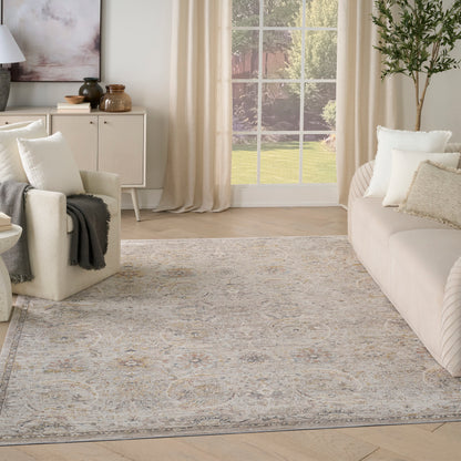 Neutral living room with large traditional-patterned area rug in gray-blue and beige, cream sofa, armchair, and tall plant.