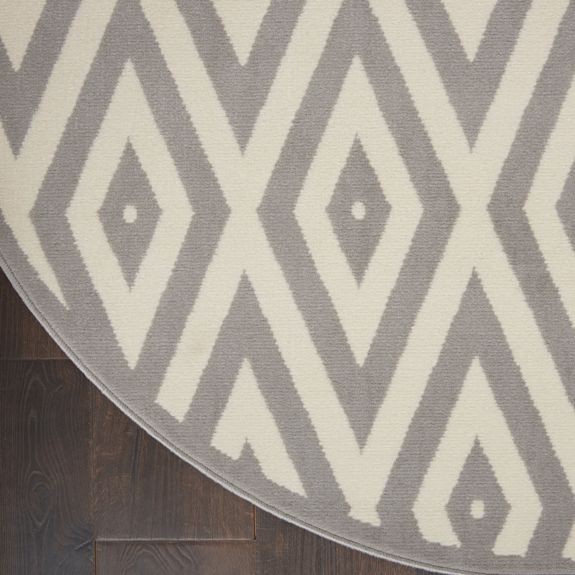 Textured gray and ivory diamond-pattern rug, round in shape, on dark hardwood floor.