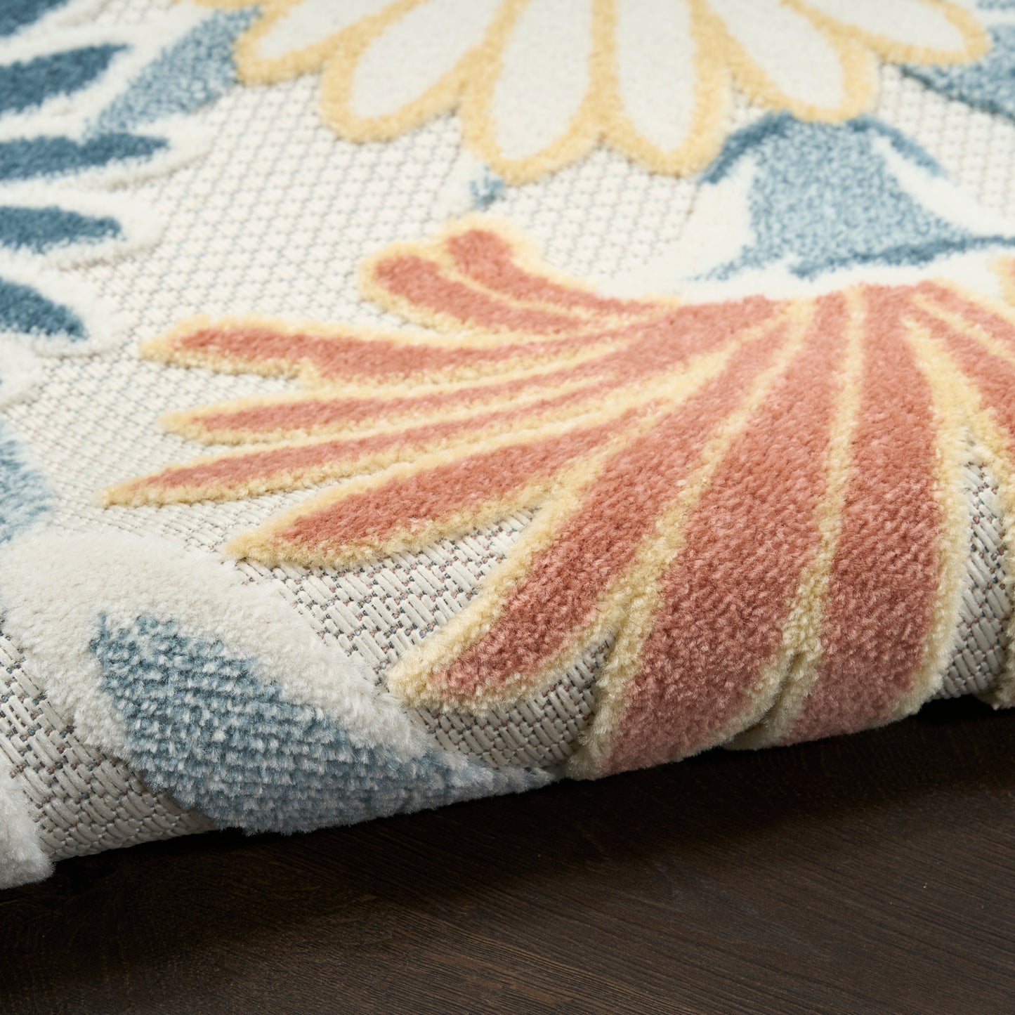 Close-up of a tufted floral rug with blue leaves and peach-pink petals on a light woven background.