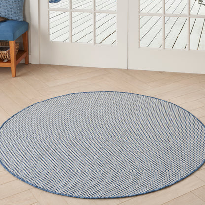 Round blue-and-white woven rug with a geometric pattern on light wood floors beside glass doors.